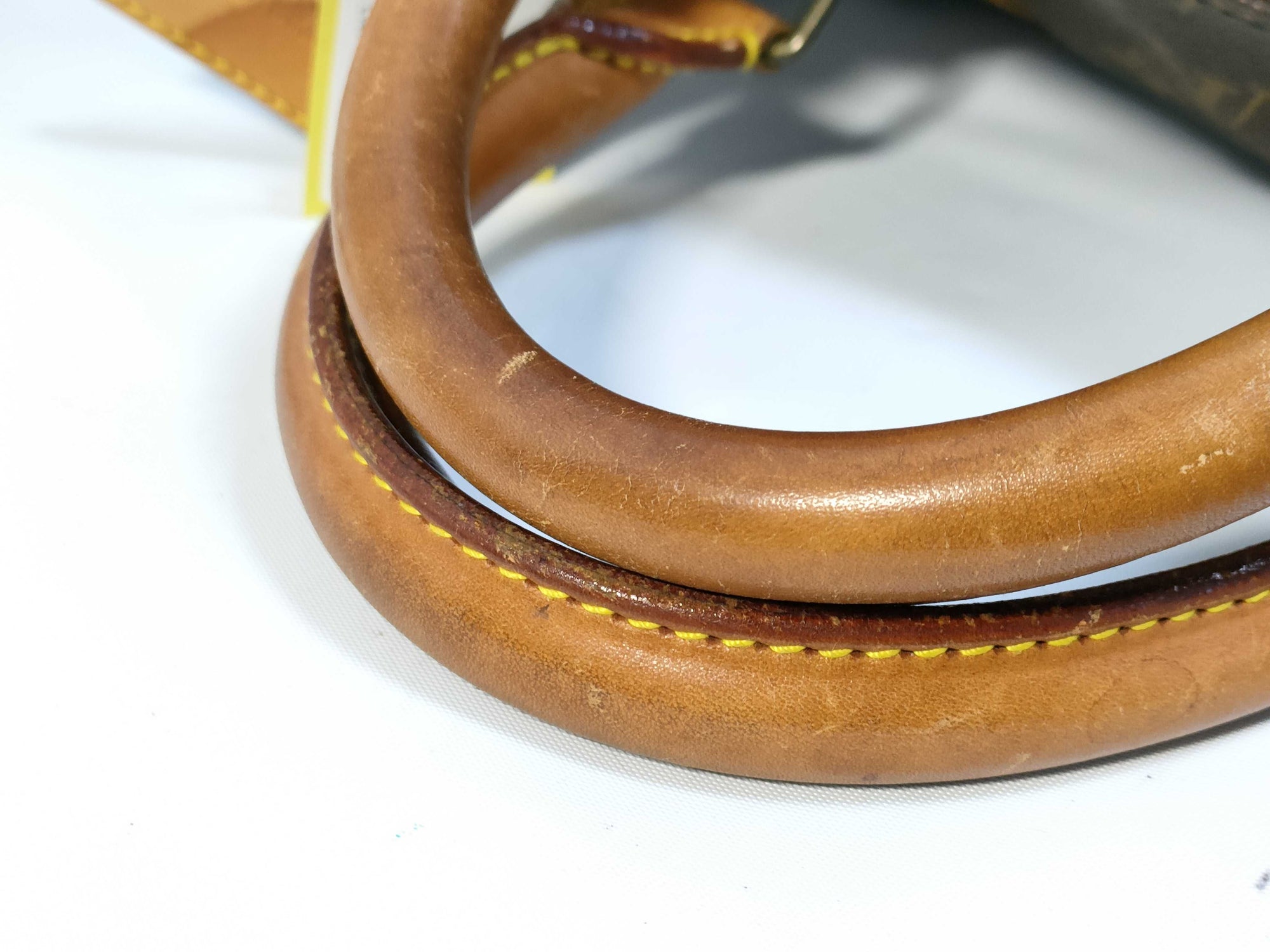 Close-up of leather handles on a vintage Louis Vuitton Keepall 55 Bandouliere travel bag showing natural patina and wear.