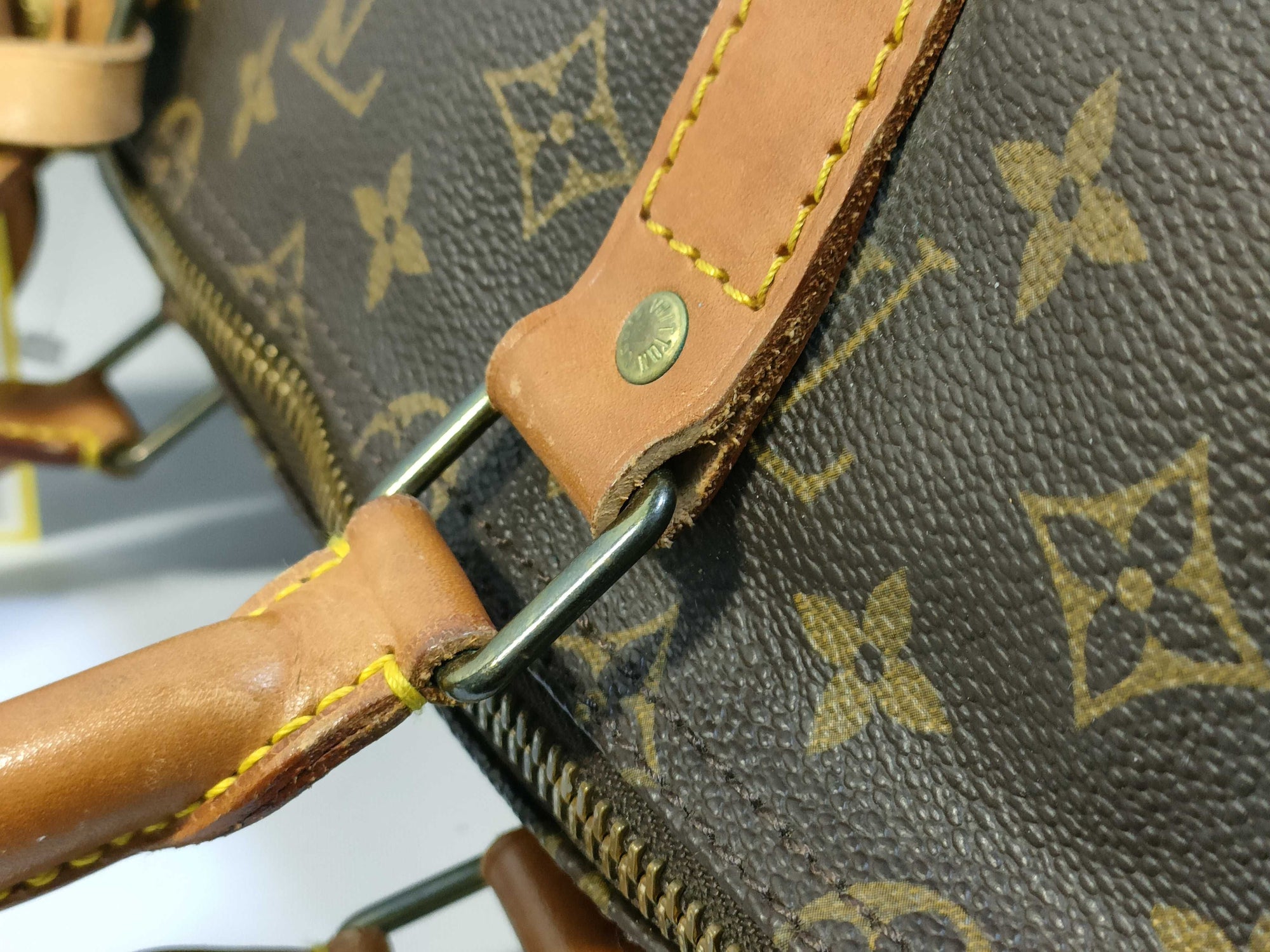 Close-up of vintage Louis Vuitton Keepall 55 monogram canvas, tanned leather handle attachment and brass hardware.