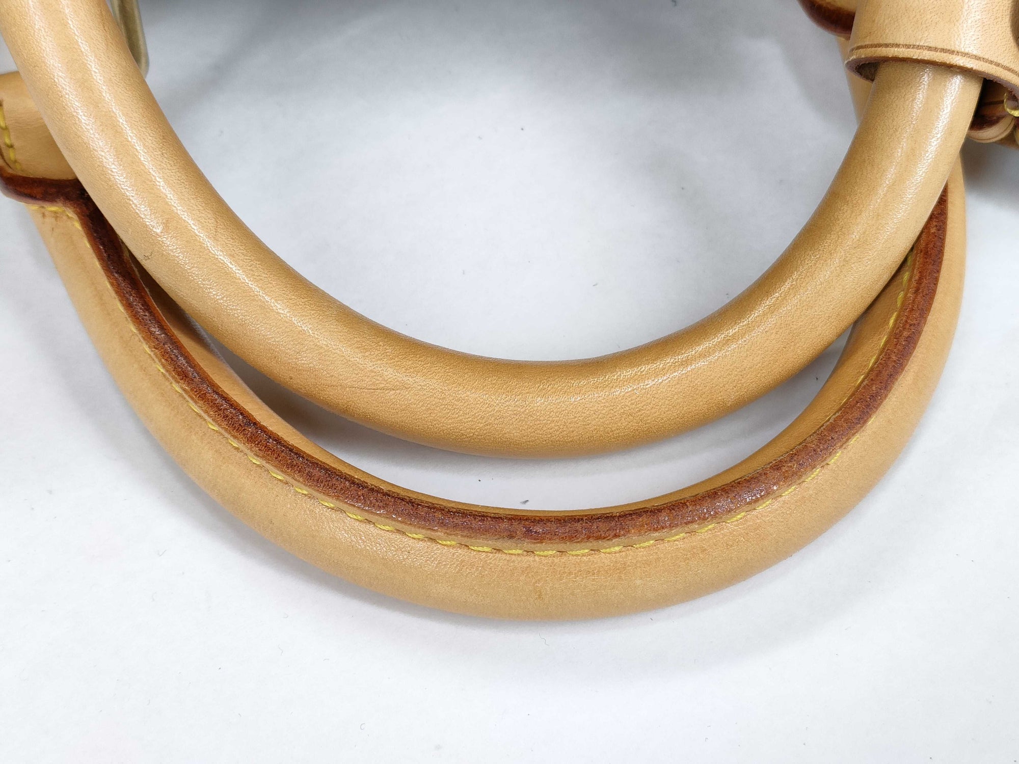 Close-up of the tanned Vachetta leather handles on a Louis Vuitton Keepall 55 travel duffle showing minor scuffs.