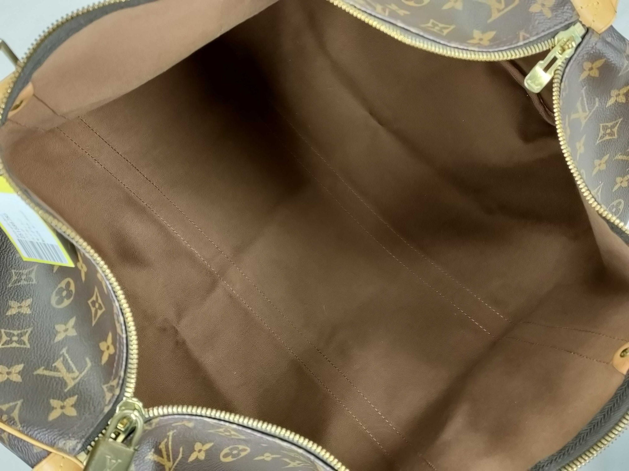 Interior of a Louis Vuitton Keepall 55 Bandouliere travel duffle showing brown canvas lining and gold-tone zippers.