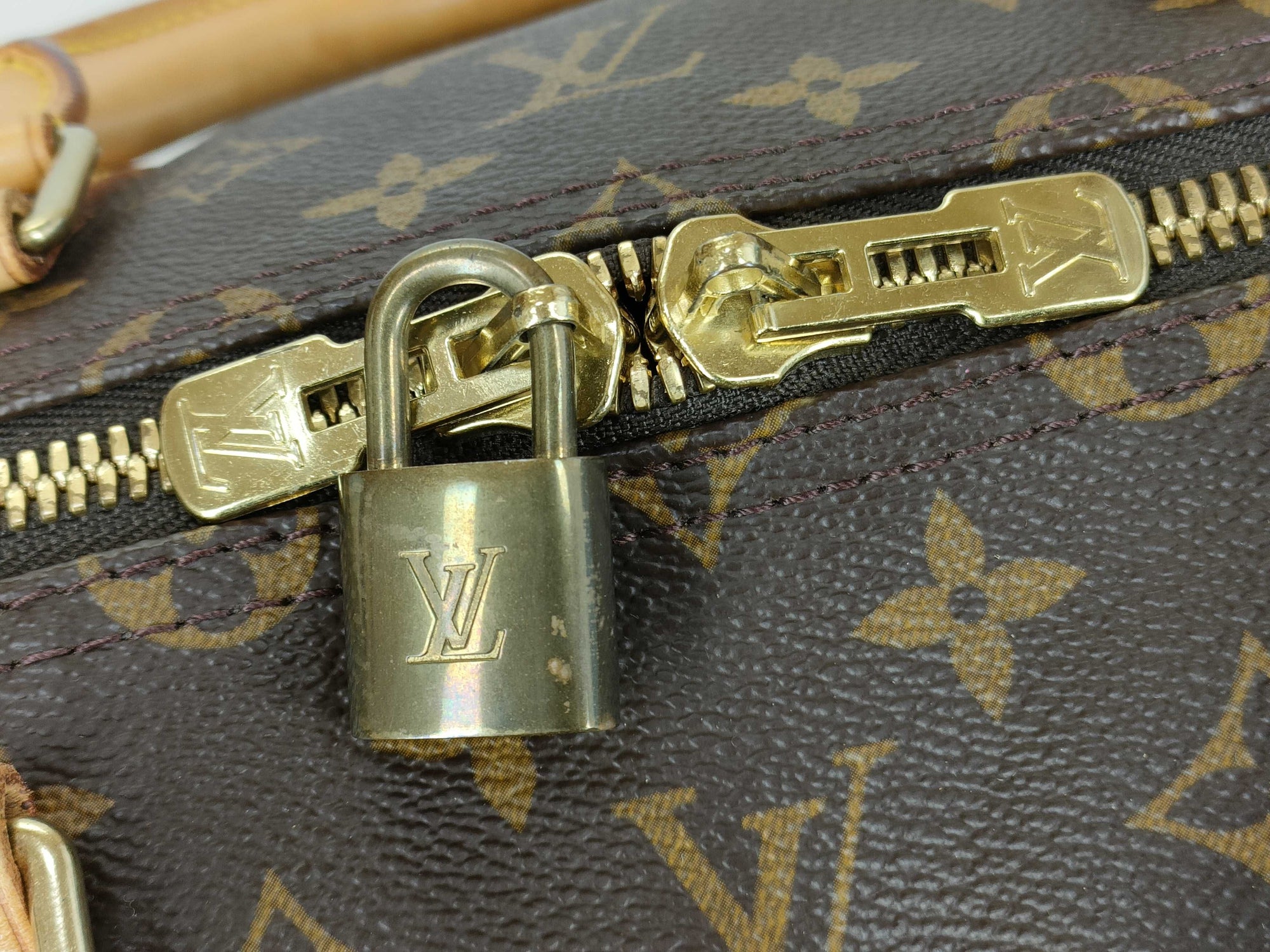 Close-up of the vintage brass LV padlock and zipper on a Louis Vuitton Keepall 55 monogram canvas travel duffle.