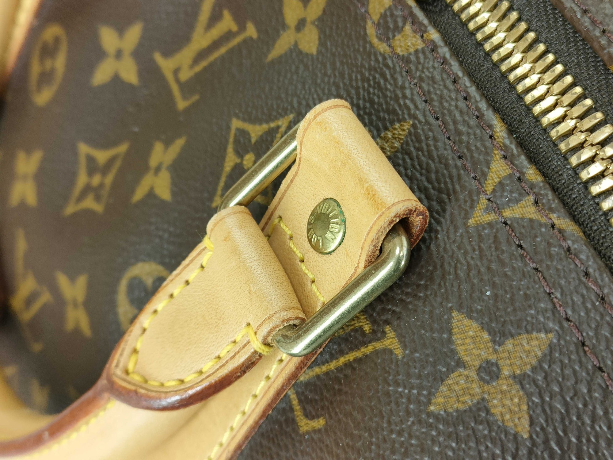 Close-up of gold-tone brass hardware and leather trim on a Louis Vuitton Keepall 55 monogram travel duffle bag.