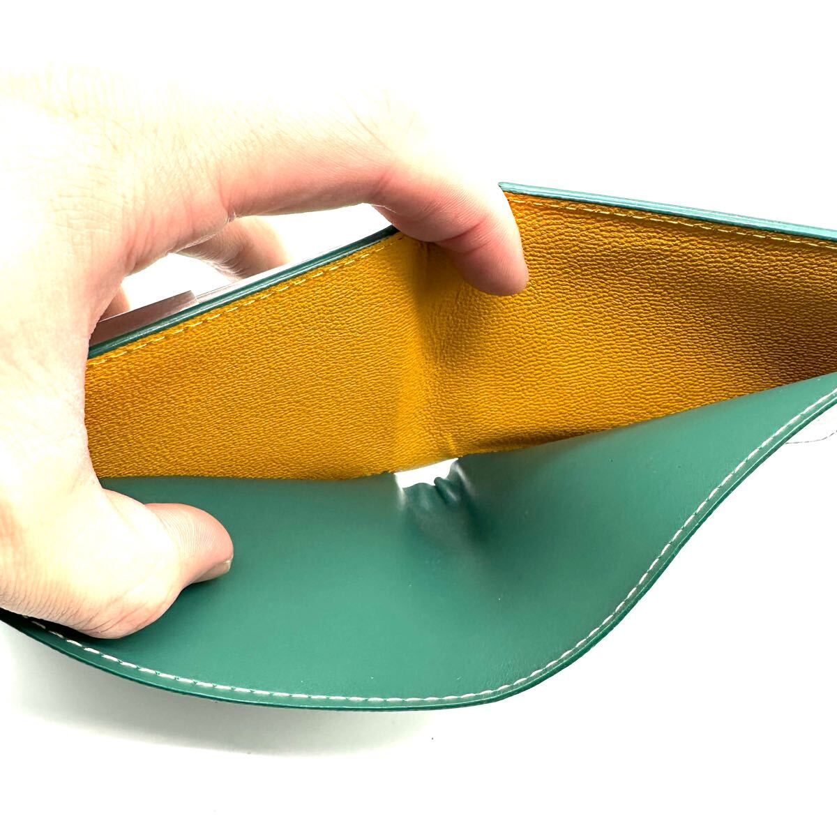 Interior bill compartment of a green Goyard Saint Florentin bi-fold wallet with yellow grained leather lining.